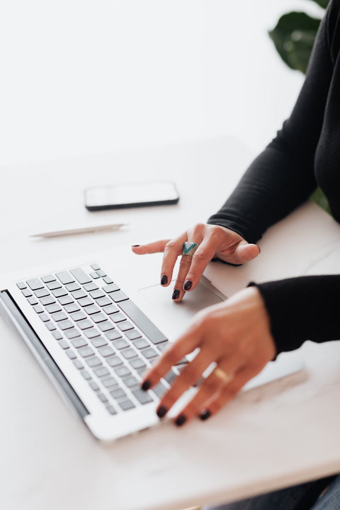 A businesswoman's hands typing on a laptop at a bright, modern workspace.